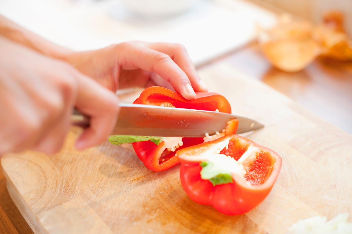 Red pepper on a cutting board with hands and a paring knife